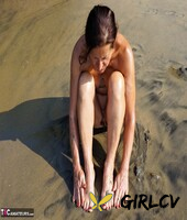 naked older woman diana ananta covers her feet in beach sand at low tide97846