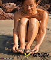 naked older woman diana ananta covers her feet in beach sand at low tide97842